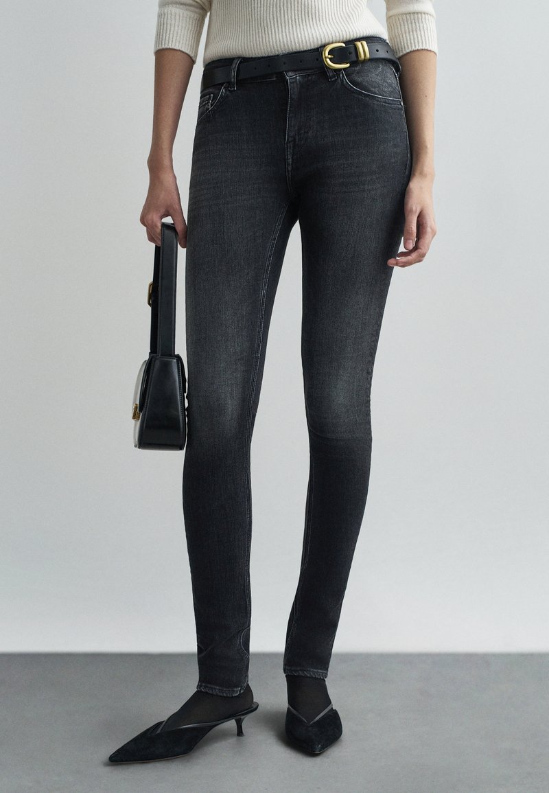 Μαύρα τζιν skinny με ελαφριά φθορά, διαθέτοντας πέντε τσέπες, βρόχους ζώνης και μια χρυσή αγκράφα, σε συνδυασμό με μυτερά μαύρα τακούνια και μια μικρή τσάντα.