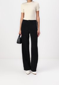 Czarne spodnie z wzorzystego korduroju o szerokich nogawkach, wysoki stan i przednie kieszenie. Połączone z dopasowaną kremową bluzką i białymi botkami na obcasie.