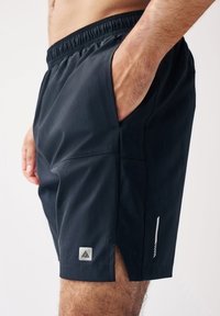 Shorts de sport noirs en tissu léger, avec des poches latérales, un logo discret et des aérations pour une meilleure respirabilité.