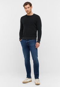 Ciemny sweter o fakturze wafelka, niebieskie dżinsy i beżowe sneakersy. Sweter ma okrągły dekolt, dopasowany krój oraz ściągacze przy rękawach i na hemie.