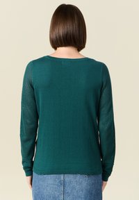 Maglione lavorato a maglia verde scuro con maniche lunghe, caratterizzato da un design a maglia aperta testurizzata sulle maniche, scollo rotondo e polsini a costine.