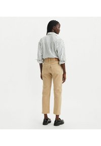 Pantalones de pana beige con pierna recta, complementados con una camisa de botones a rayas con mangas remangadas. Zapatos negros de tipo slip-on.