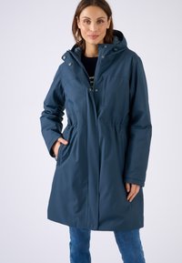 Cappotto blu resistente all'acqua con cappuccio, vita affusolata, maniche lunghe e tasche laterali. Presenta una chiusura con zip e un design semplice.