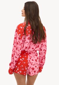 Ensemble chemise et short à motifs floraux dans des tons roses et rouges, avec des motifs floraux variés. Tissu doux, coupe ample et détails à boutons sur les manches.