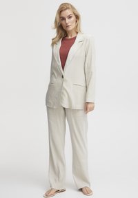 Leinenanzug in hellbeige mit einem Blazer mit einem Knopf und weitem Bein. Kombiniert mit einem weinroten Oberteil und flachen Sandalen, mit einem entspannten Schnitt.
