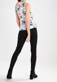 Floral peplum-toppi, jossa on monivärinen kukkakuosi pinkin ja vihreän sävyissä, yhdistettynä kapeisiin mustiin housuihin ja nilkkureihin.