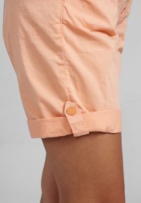 Shorts de algodón melocotón con dobladillo enrollado, que presentan un detalle de botón en el costado y una textura suave.