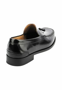 Mocasín de cuero negro con tacón bajo, puntera redondeada y costuras decorativas a lo largo de la parte superior. Acabado suave con un interior marrón en contraste.
