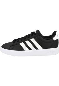 Zapatillas negras de material sintético con diseño de tres rayas blancas, cuello acolchado y suela blanca de goma. Logotipo en la lengüeta y en el talón.