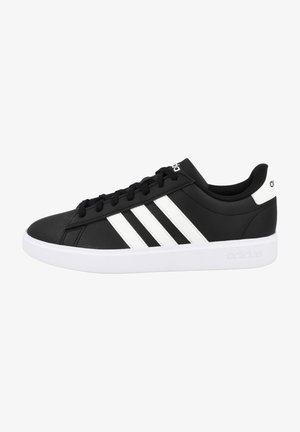 Zapatillas negras de material sintético con diseño de tres rayas blancas, cuello acolchado y suela blanca de goma. Logotipo en la lengüeta y en el talón.