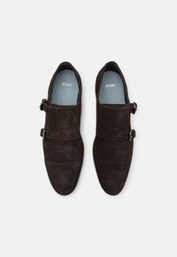 Chaussures en daim marron foncé avec une texture lisse, dotées de deux boucles métalliques et d'un design épuré. Semelles intérieures de couleur bleu clair visibles à l'intérieur.