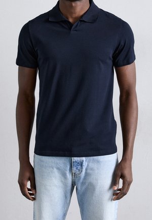 Polo bleu marine en coton doux, doté d'un col classique et de manches courtes, assorti à un jean en denim bleu clair.