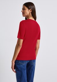 Röd kortärmad t-shirt av mjuk bomull, med en klassisk rund halsringning. Kombineras med blå denimjeans som har en avslappnad passform.
