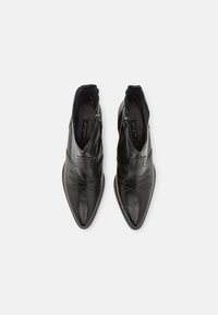 Botas de cuero negro hasta el tobillo con puntas afiladas, costuras decorativas y cierre con cremallera. Textura suave, forro blando y un diseño elegante.