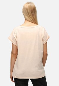 Světle růžové tričko s volným střihem, srolovanými krátkými rukávy a širokým výstřihem. Hladká textura, rovný lem a minimální design.