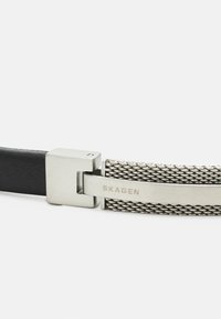 Bracciale in pelle nera e rete in metallo argentato con una chiusura rettangolare in metallo con il nome del marchio "SKAGEN" inciso.