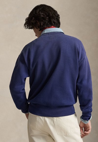 Sudadera azul marino con cuello redondo, mangas largas, puños y dobladillo acanalados, tejido texturizado. Camisa azul claro con cuello visible debajo.