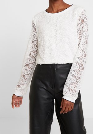 Witte kanten top met lange mouwen, een ronde halslijn en bloemmotieven. Gecombineerd met zwarte leren broek, met een gladde textuur.