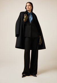 Zwarte wollen jas over een op maat gemaakt zwart krijtstreep pak, gecombineerd met een lichtblauw shirt en olijfgroene handschoenen. Puntige zwarte hakken.