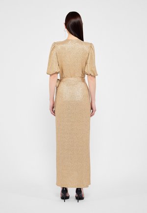 Frau mit langen dunklen Haaren, die ein gold schimmerndes Kleid mit Puffärmeln und schwarze High Heels trägt, von hinten gezeigt.