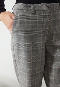 Pantalons à carreaux gris, avec un motif à damier composé de fines lignes noires et rouges. Taille mi-haute avec poches latérales. Fabriqué en tissu texturé.