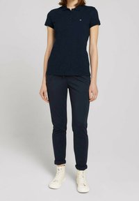 Marinblå pikétröja med kort ärm och tre knappar i knäppningen, i kombination med slim fit marinblå byxor och vita högtoppsskor.