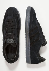 Baskets en daim noir avec une finition texturée, dotées de trois rayures sombres, d'un bout rond, d'un laçage à l'avant et d'une semelle en caoutchouc.