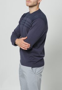 Navy crew neck sweater with a textured upper section and horizontal stripes, made from a soft fabric, featuring ribbed cuffs and hem.