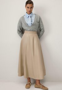 Beežist nahast A-lõikelise seelik kõrgema vöökohaga, kombineeritud halli üleuuritud kampsuni ja helesinise lipsuga. Pehme tekstuur, minimalistlik disain.