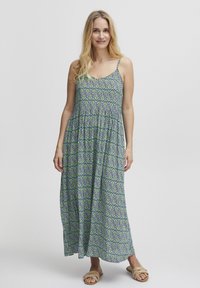 Robe maxi avec un motif floral bleu et vert, en tissu l�éger, bretelles spaghetti, taille élastiquée, coupe décontractée, portée avec des sandales à talons beiges.