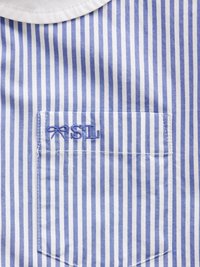 Krátký rukáv košile s modrými a bílými vertikálními pruhy, kulatým límcem a malou náprsní kapsou s vyšitými iniciálami.