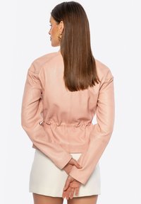 Giacca in pelle rosa chiaro con vita stretta, maniche lunghe e texture liscia. Vista posteriore che mette in mostra un design aderente e una decorazione minimale.