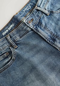 Voľné džíny z denimu v svetlomodrej farbe s vyblednutou textúrou. Obsahujú oranžové šitie, zapínanie na gombík a dizajn s piatimi vreckami.