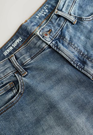 Gaiši zili, plata piegriezuma džinsi ar nolietotu tekstūru. Iekļauj oranžu diegu, pogas aizdari un piecu kabatu dizainu.