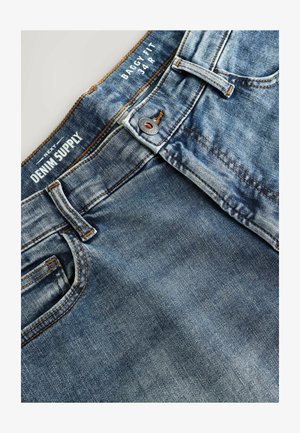 Luźne dżinsy w jasnoniebieskim kolorze z wyblakłą fakturą. Posiadają pomarańczowe przeszycia, zapięcie na guzik oraz pięć kieszeni.