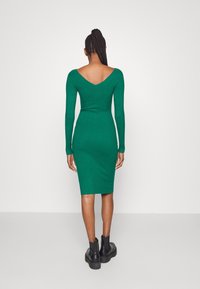 Zelené žebrové dlouhé šaty s hlubokým výstřihem na zádech, přiléhavý silueta a délka po kolena. V kombinaci s černými robustními kotníkovými botami na podpatku.
