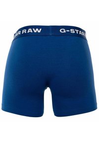 Boxers azules hechos de una tela suave, con una cinturilla elástica ancha que presenta el logo "G-Star RAW" en blanco. Textura suave y diseño ajustado.