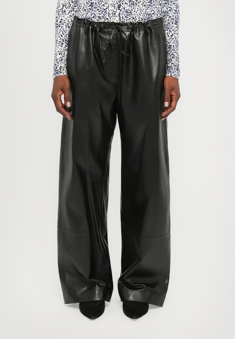 Black leather trousers with a wide fit, featuring a drawstring waist and smooth texture. Paired with black pointed shoes.