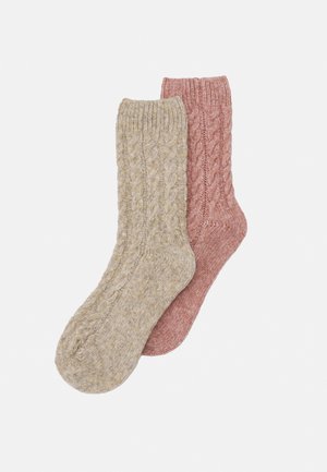 Zwei Paar gestrickte Socken: eines in Beige mit Zopfmuster, das andere in sanftem Rosa mit glatter Oberfläche. Beide besitzen gerippte Bündchen.