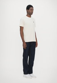 Kremfarget bomulls t-skjorte med rund hals, sammen med mørkeblå denimjeans og hvite joggesko. Enkel design, ingen utsmykninger.