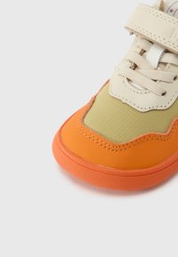 Αθλητικό παπούτσι με συνδυασμό μπεζ, πράσινου και πορτοκαλί υλικών, με υφασμένη επιφάνεια στο πάνω μέρος και ανθεκτική σόλα από καουτσούκ. Κλείνει με λουράκι βέλκρο.