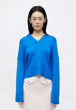 Niebieski sweter z dzianiny z dekoltem w serek i długimi rękawami, z prążkowanymi mankietami i dołem. Połączony z jasnoróżową spódnicą z detalami kieszeni.