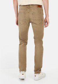 Beige jeans met een slim fit, achterzakken met diamantsteek en een leren label op de tailleband. Gecombineerd met witte sneakers.