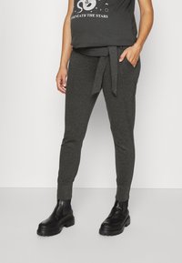 Grå joggers med knytmidja, smalnande ben och framfickor, tillsammans med svarta ankelboots. Slät textur och avslappnad design.