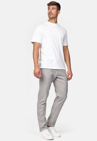 Camiseta de algodón blanca combinada con pantalones gris claro. El modelo lleva zapatillas blancas, mostrando un estilo casual y relajado.