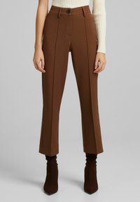 Brązowe, dopasowane spodnie z talią o średnim stanie, z przodu zakładki i prostym krojem; posiadają pojedyncze zapięcie na guzik i gładką fakturę.