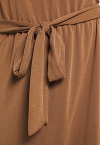 Robe marron avec une ceinture en tissu, présentant une texture douce et une taille froncée. Le matériau semble élastique et léger.