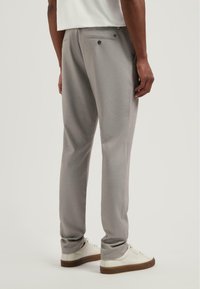 Grijze broek van een gestructureerde stof, met achterzakken en een slim fit. Draagt met witte sneakers, wat zorgt voor een strakke, moderne uitstraling.