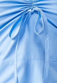 Hele sinine topp, millel on kokku kogutud kangas ja seotud lipsu detail. Omab siledat tekstuuri ning delikaatset õmblust servades.