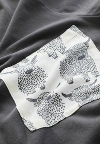 Katoenen t-shirt in donkergrijs met een witte patch die een herhaald patroon van gestileerde zwarte dieren toont. Zachte textuur en casual ontwerp.